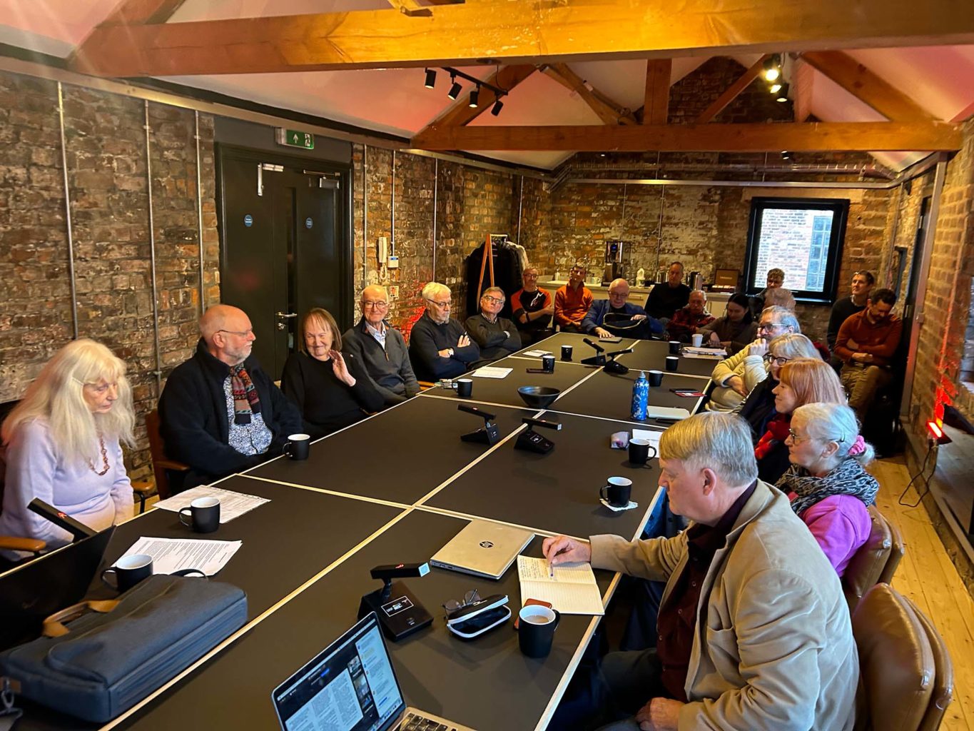 Image depicts group of people sitting round a board table in a historic setting